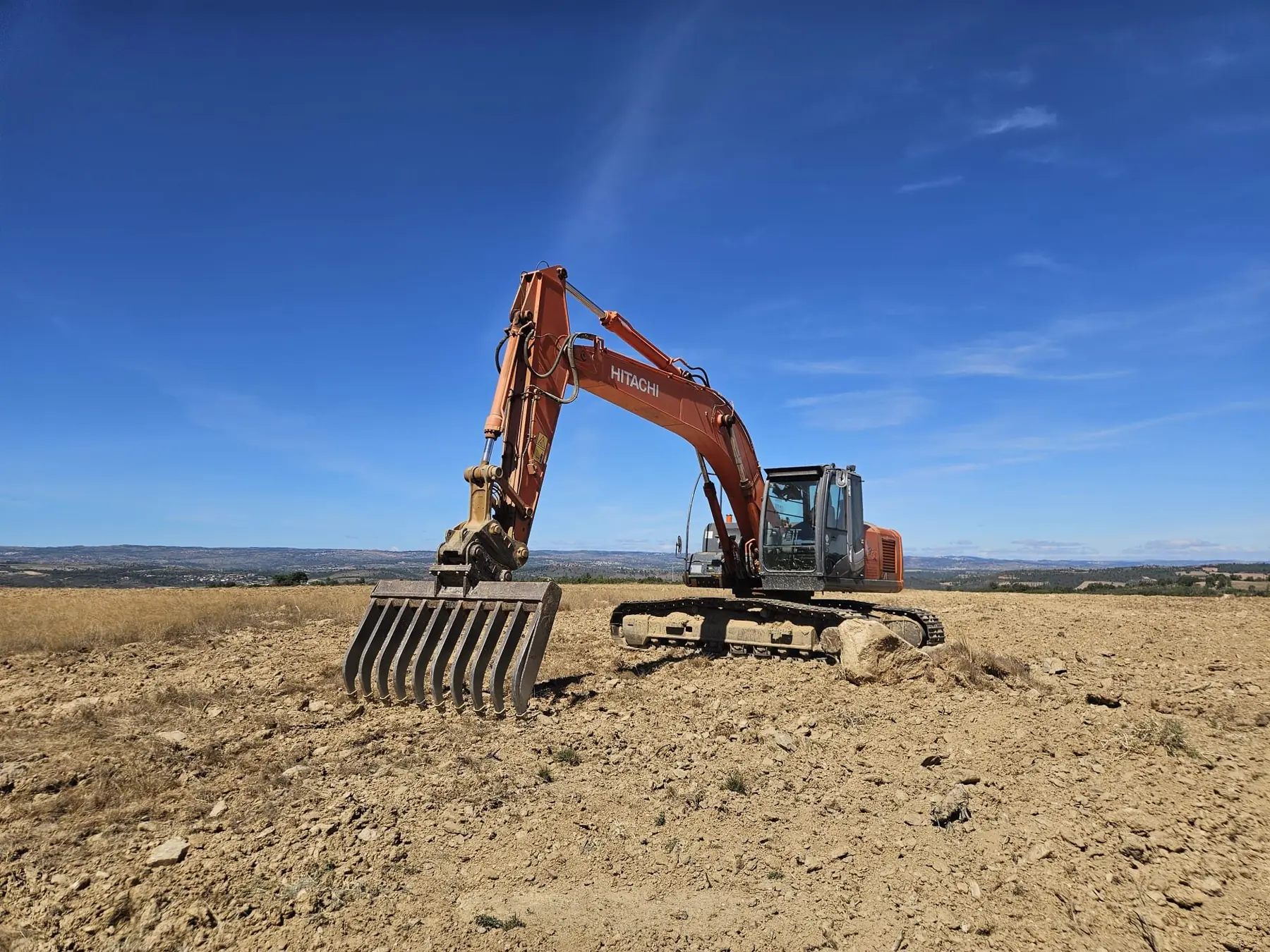 An excavator with a root rake preparing bare ground for planting.