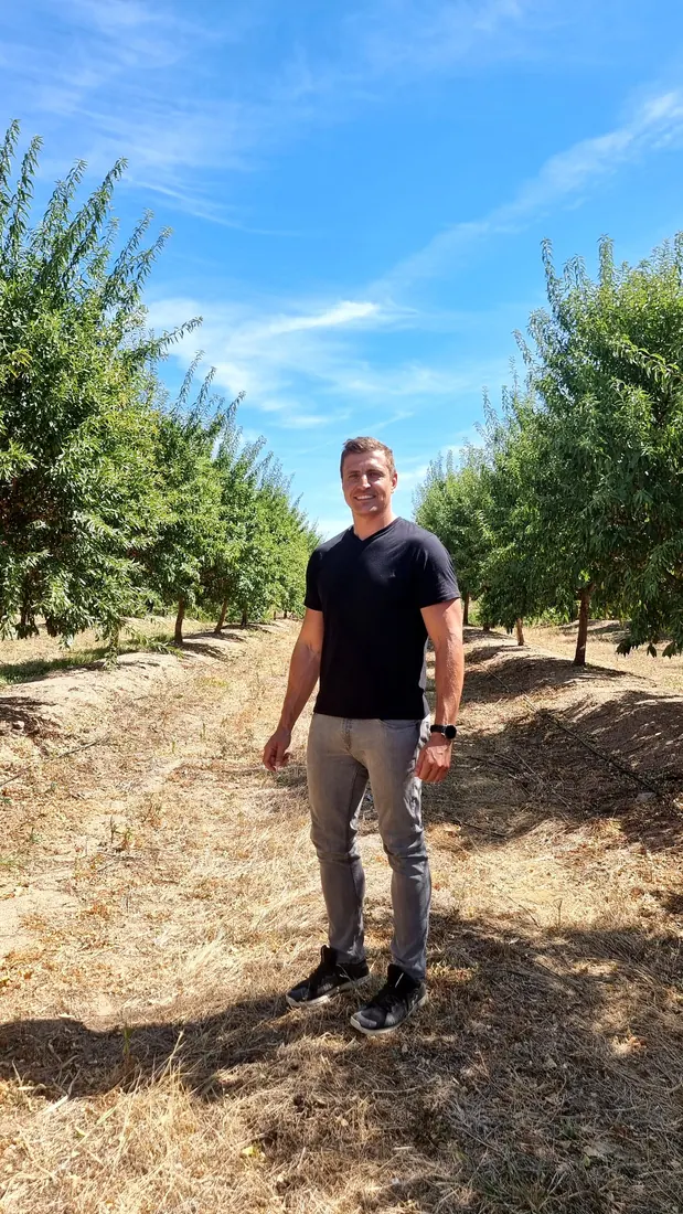 Jacques Naudé, founder of Joseph’s Dream, standing in a sunlit orchard row.