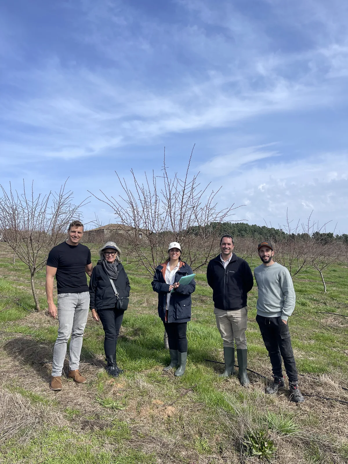 A small group standing together in a young almond orchard on a spring day.